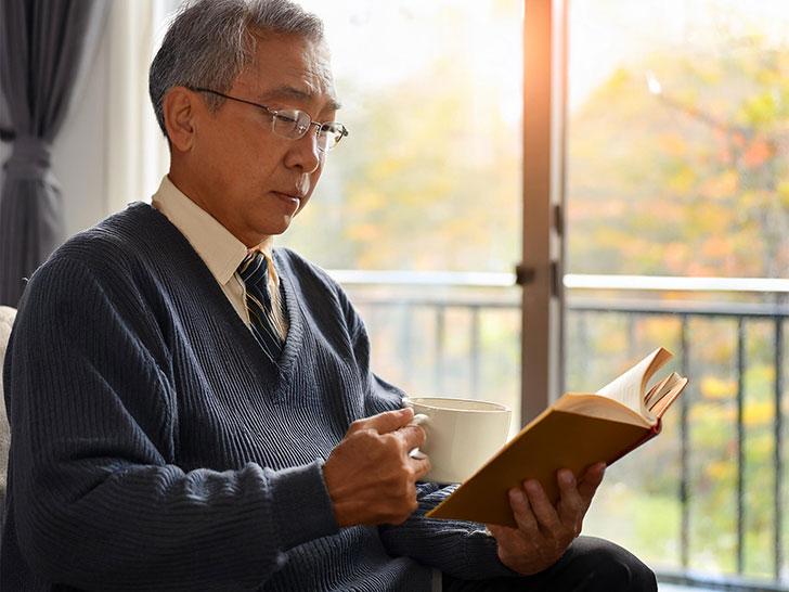 コーヒーを飲みながら読書をするシニア男性