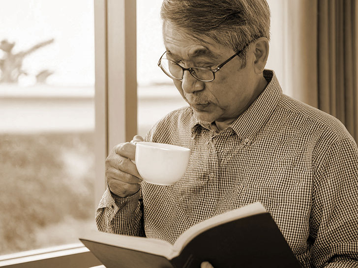 コーヒーを飲みながら読書をするシニア男性