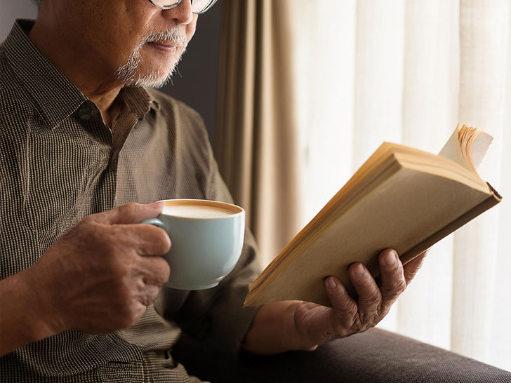 コーヒーを飲みながら読書をするシニア男性