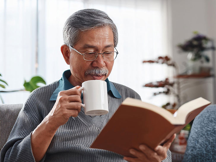 コーヒーを飲みながら読書をするシニア男性