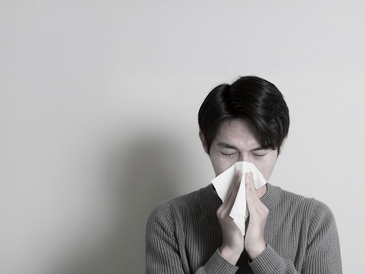 ティッシュで鼻をかむ若い男性