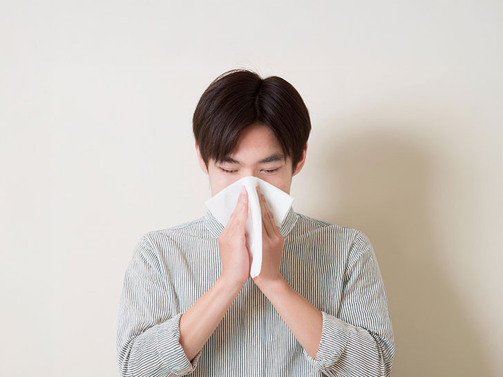 ティッシュで鼻をかむ若い男性