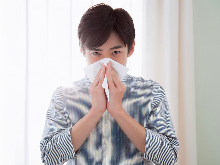 ティッシュで鼻をかむ若い男性