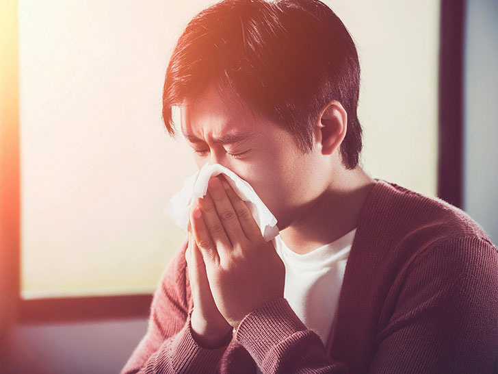 ティッシュで鼻をかむ若い男性