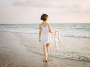 白いドレスで海岸を歩く若い女性