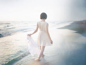 白いドレスで海岸を歩く若い女性