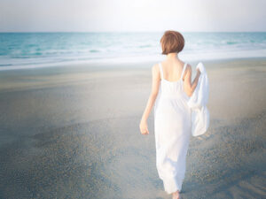 白いドレスで海岸を歩く若い女性