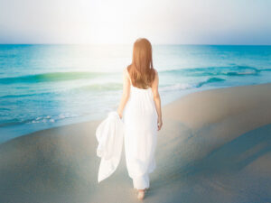 白いドレスで海岸を歩く若い女性