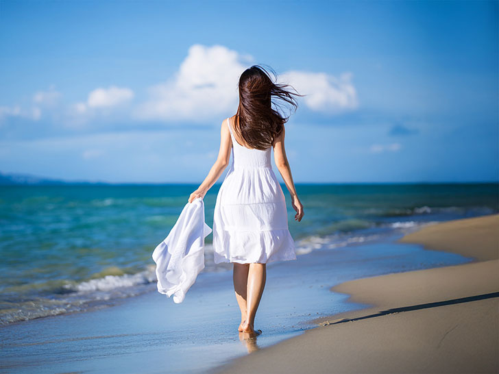 白いドレスで海岸を歩く若い女性
