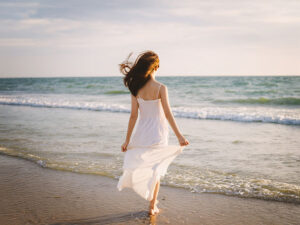 白いドレスで海岸を歩く若い女性