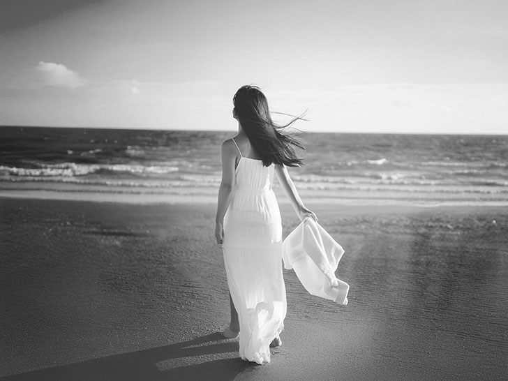 白いドレスで海岸を歩く若い女性