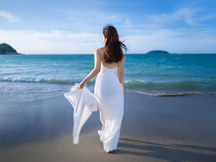 白いドレスで海岸を歩く若い女性