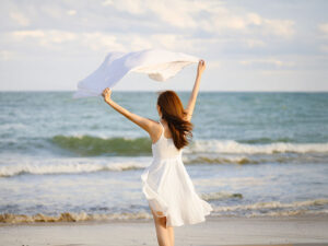 白いドレスで海岸を歩く若い女性