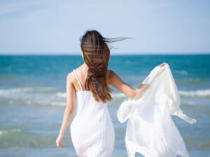 白いドレスで海岸を歩く若い女性