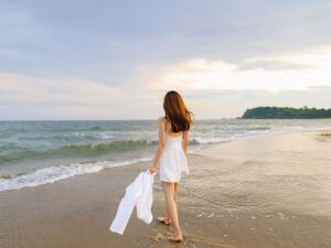 白いドレスで海岸を歩く若い女性