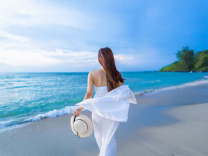 白いドレスで海岸を歩く若い女性