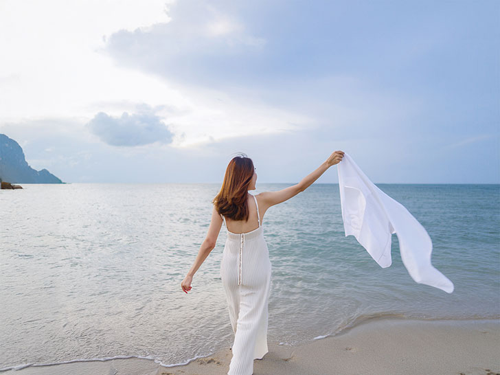 白いドレスで海岸を歩く若い女性