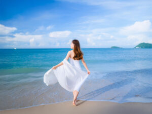 白いドレスで海岸を歩く若い女性