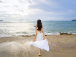 白いドレスで海岸を歩く若い女性