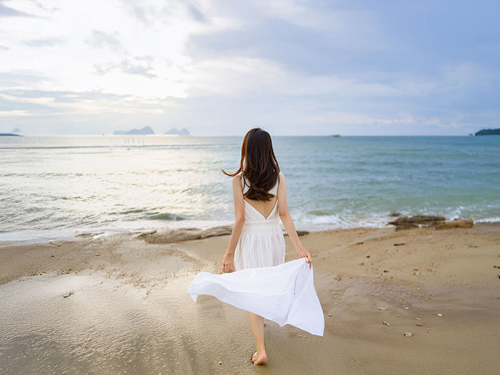 白いドレスで海岸を歩く若い女性