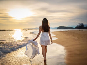 白いドレスで海岸を歩く若い女性